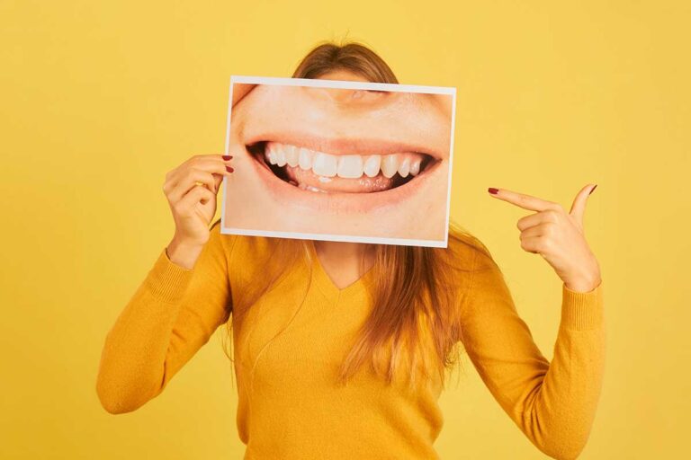young-woman-holding-pointing-finger-picture-mouth-smiling-showing-her-teeth-yellow-background-dentist-concept